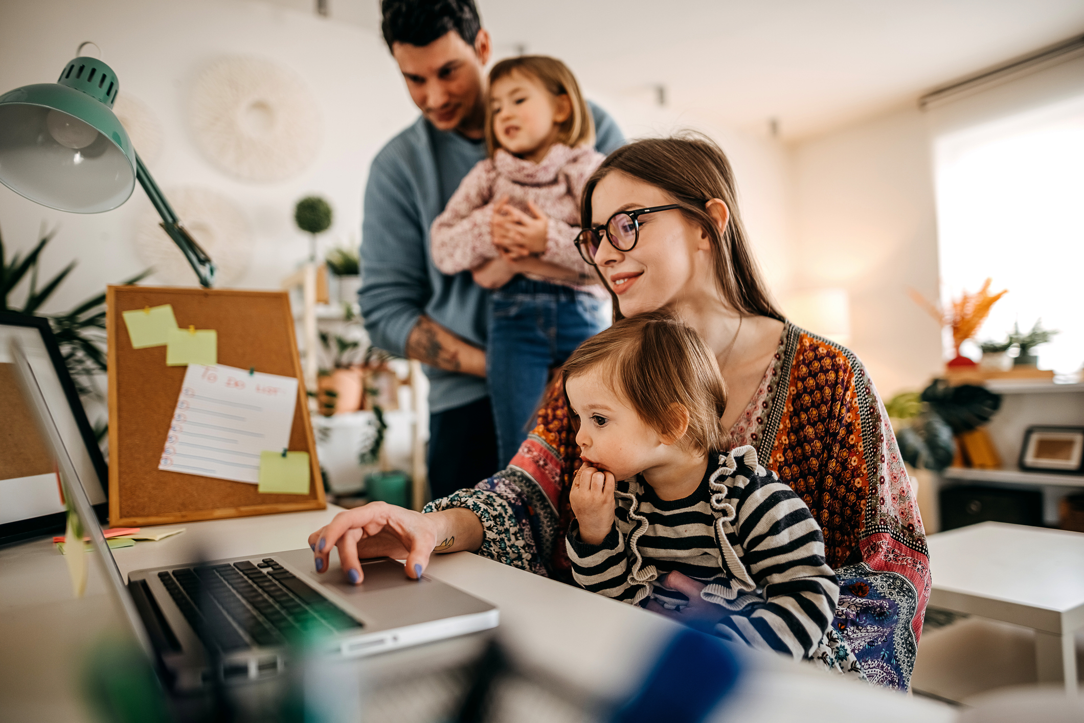 Eine Mutter und ein Vater sind mit zwei kleinen Kindern zuhause und arbeiten am Laptop. 
