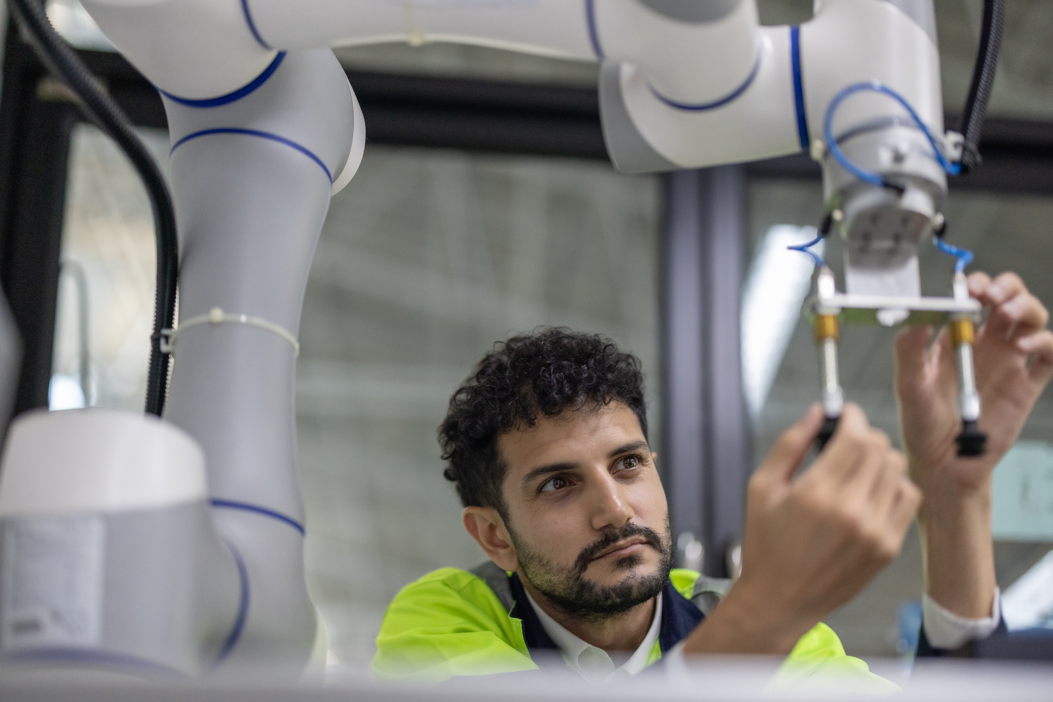 Mann und justiert mit beiden Händen einen Greifer an einem industriellen Roboterarm